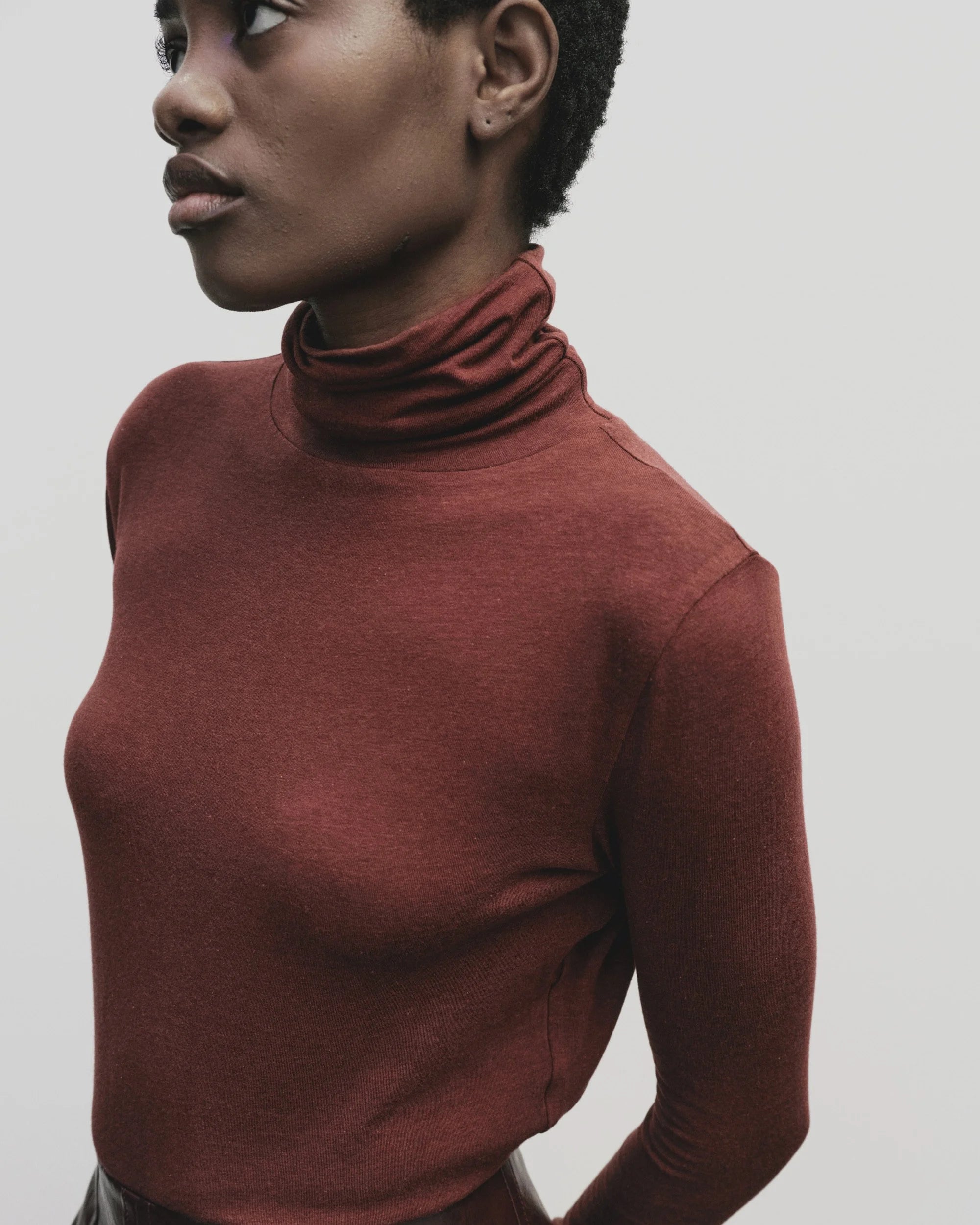 Person wearing a brown turtleneck sweater against a plain background