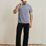 Person wearing a gray t-shirt, black pants, and a white cap with text on a wooden floor.