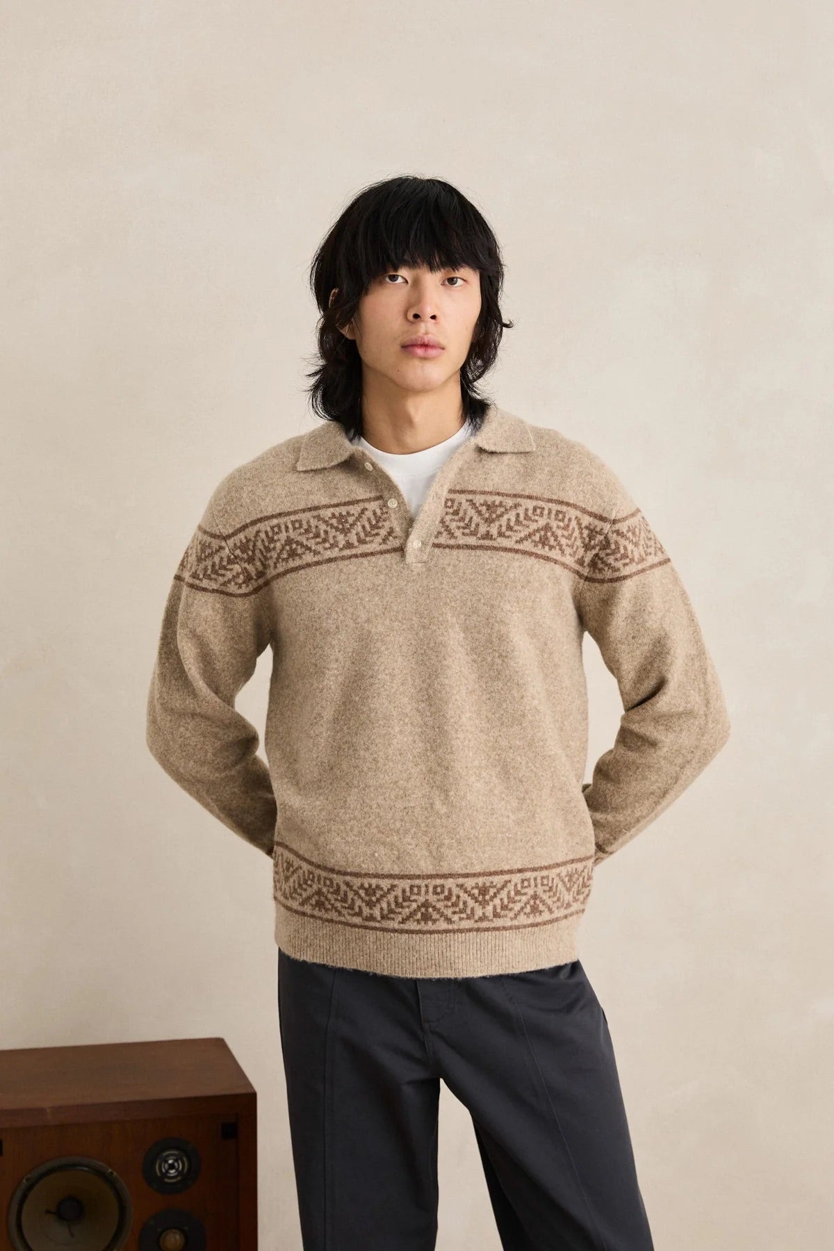 Man wearing a beige knitted sweater with patterned details against a plain background
