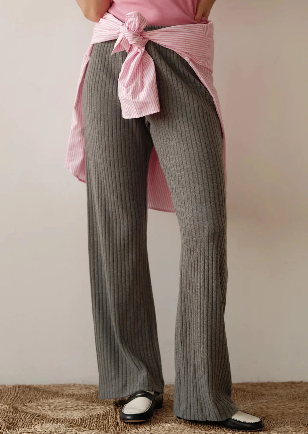 An image of the bottom half of a model wearing the Sweater Rib Simple Pants in Charcoal styled with a pink blouse tied around her waist