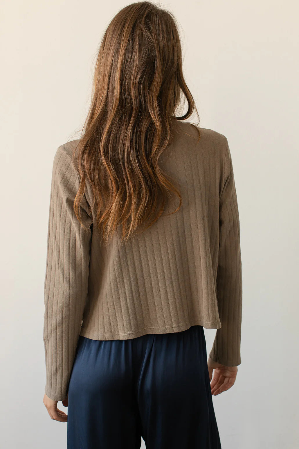 A medium shot image of the back of a female model wearing the Pointelle Cardigan styled with a navy pant