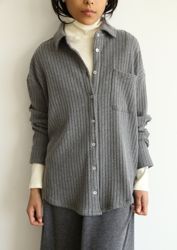 A medium shot image of a female model wearing the Sweater Rib Button Down in Charcoal Grey styled over a cream turtleneck and a charcoal grey skirt