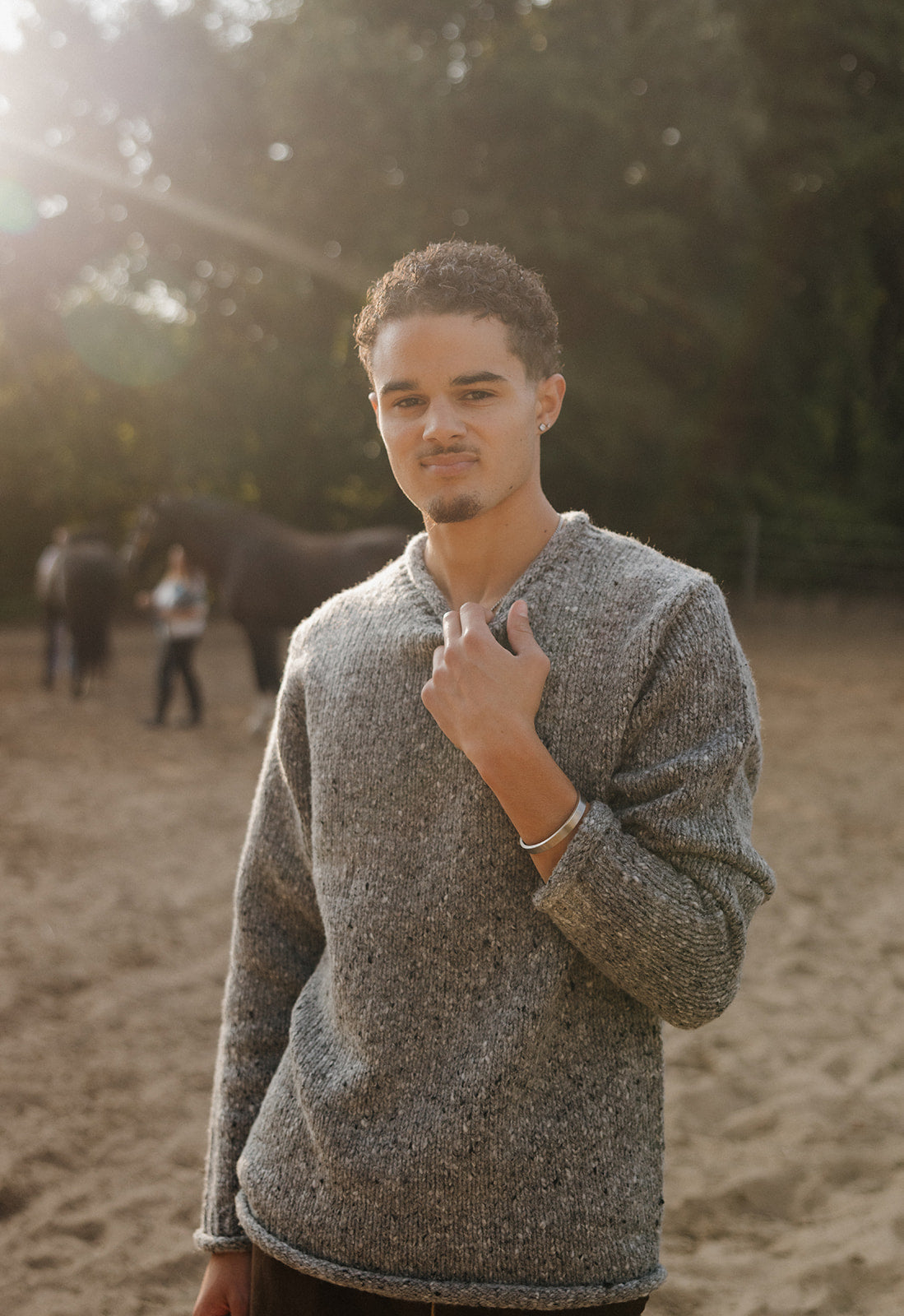 Man wearing a gray sweater standing outdoors with trees in the background
