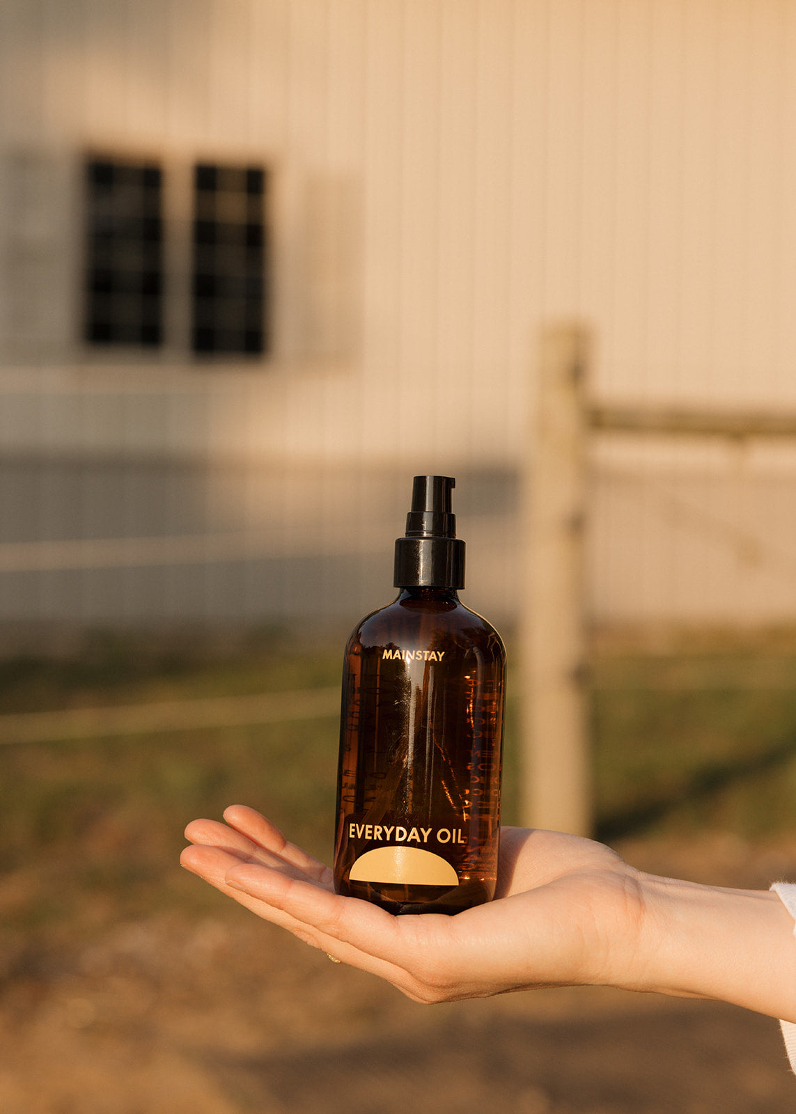 Hand holding a bottle of 'Everyday Oil' by Mauvejay outdoors.