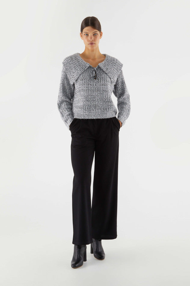 A full body image of a female model standing with her hands in her pockets while wearing the Collar Lace-up Sweater styled with a black trouser and boot. 