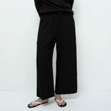 Person wearing black wide-leg pants and a black top on a white background