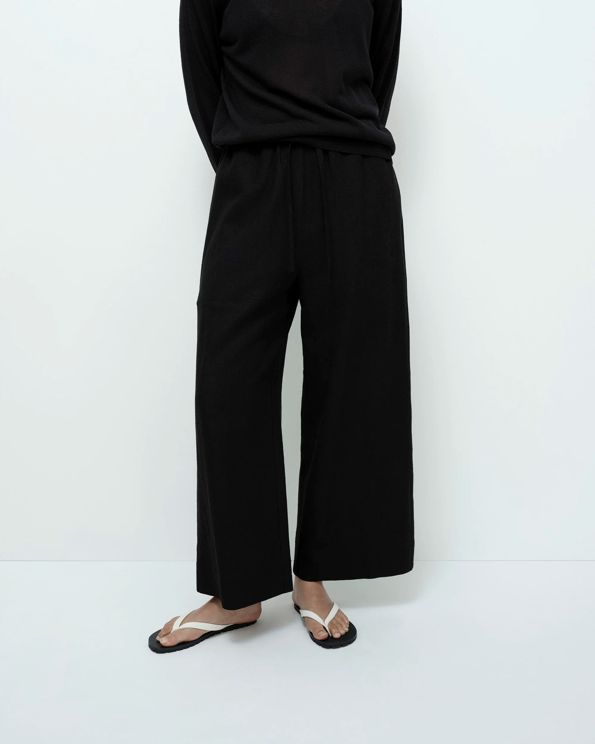 Person wearing black wide-leg pants and a black top on a white background