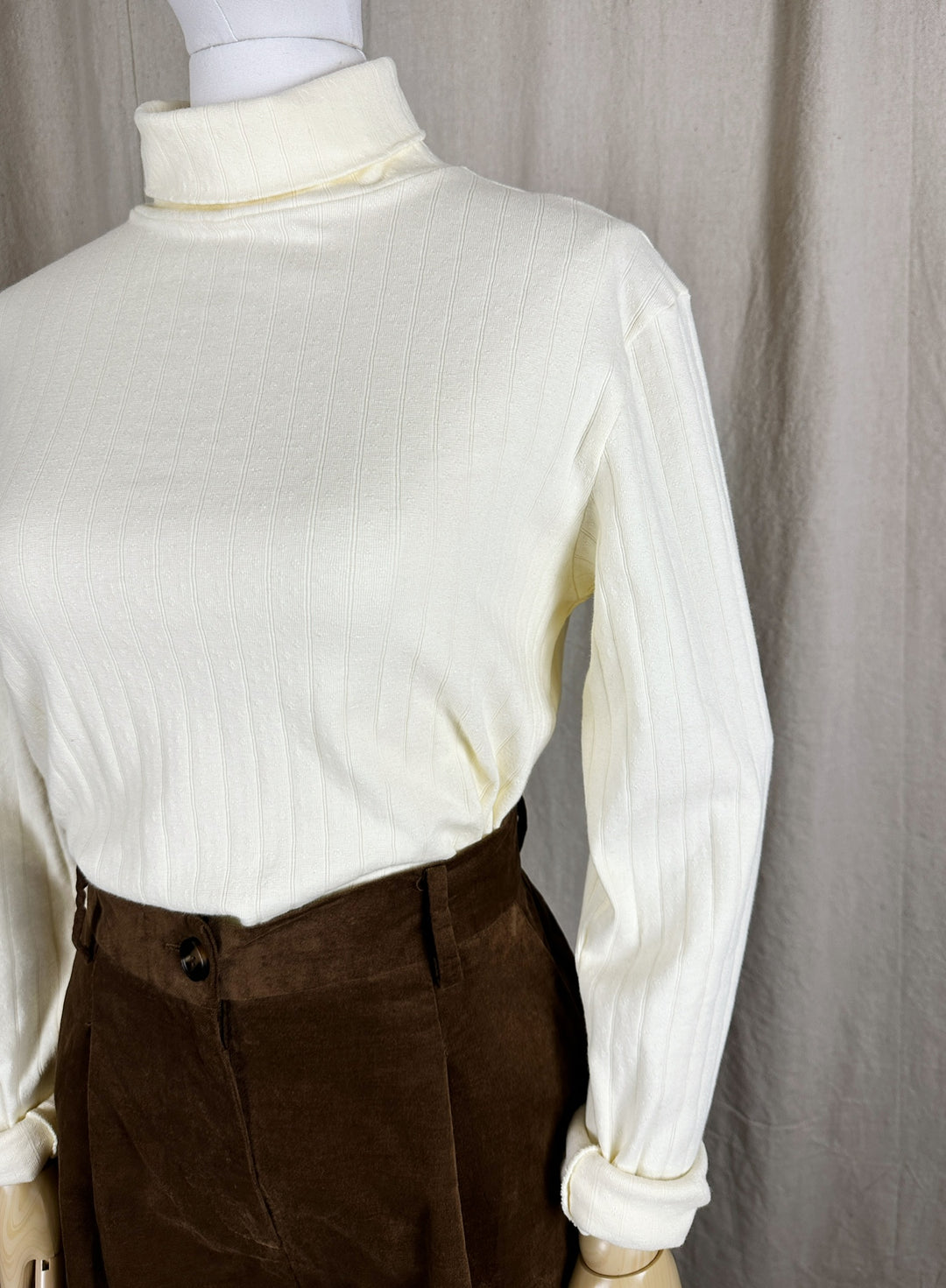A close up detail image of the Pointelle Turtleneck styled tucked into a brown pant on a mannequin