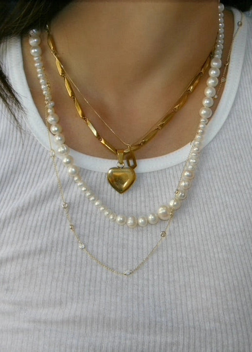 Pearl necklace with a gold heart pendant worn by a person on a white background