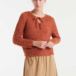 Woman wearing a rust-colored knitted sweater with a white background