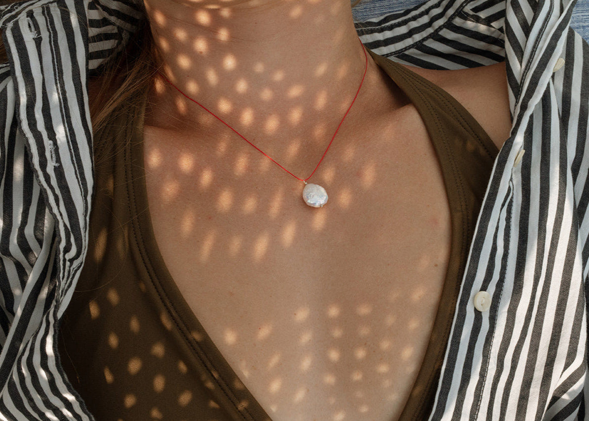 Necklace with a pendant worn by a person, with a patterned shirt and light filtering through.