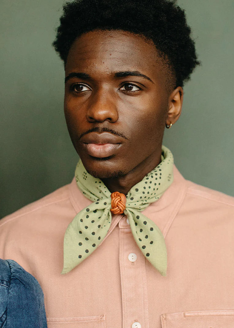 Man wearing a light pink shirt with a green patterned scarf against a green background