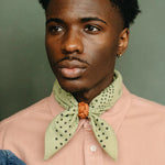 Man wearing a light pink shirt with a green patterned scarf against a green background