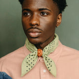 Man wearing a light pink shirt with a green patterned scarf against a green background