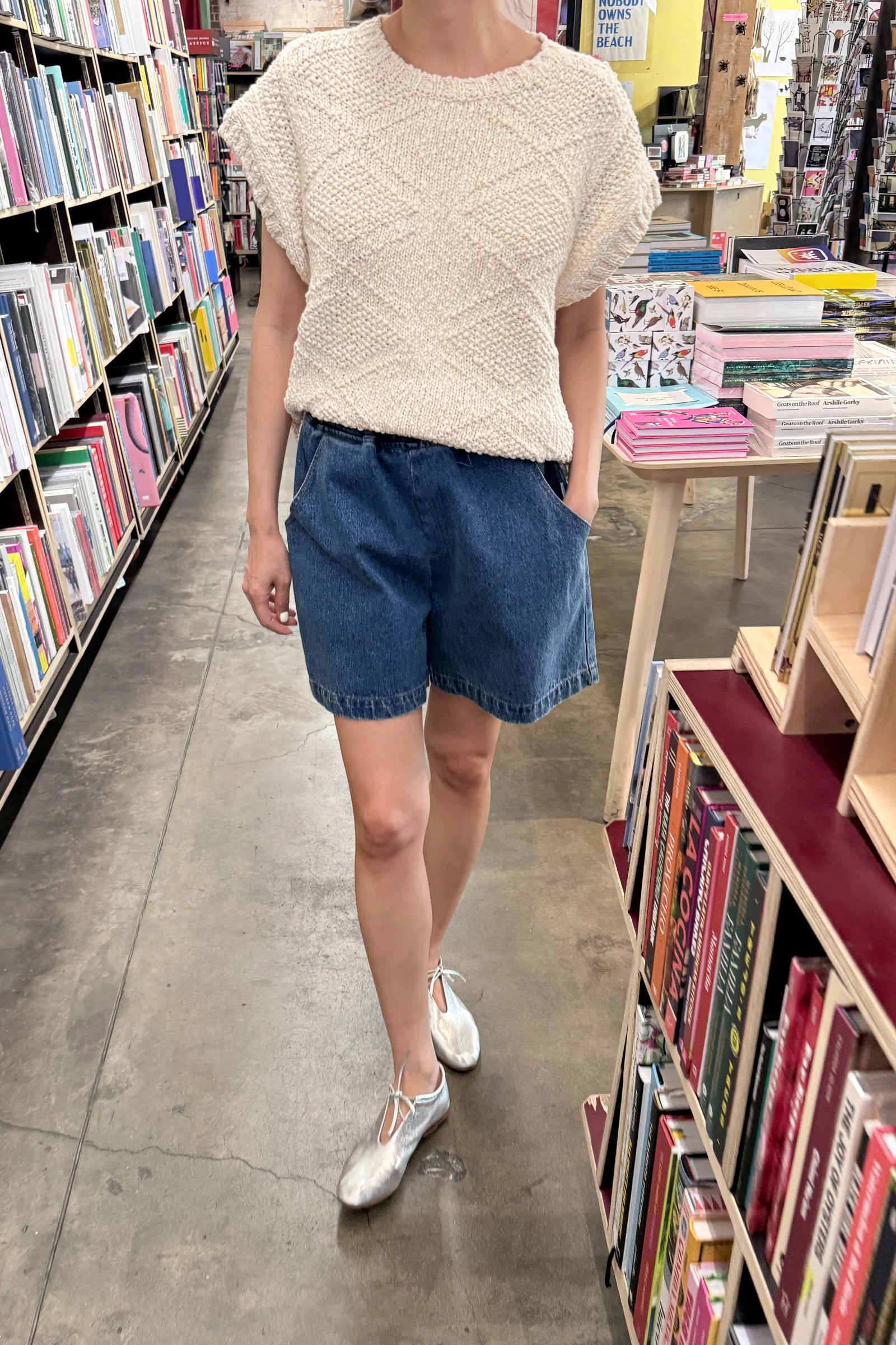 Person wearing a white top and blue shorts in a bookstore