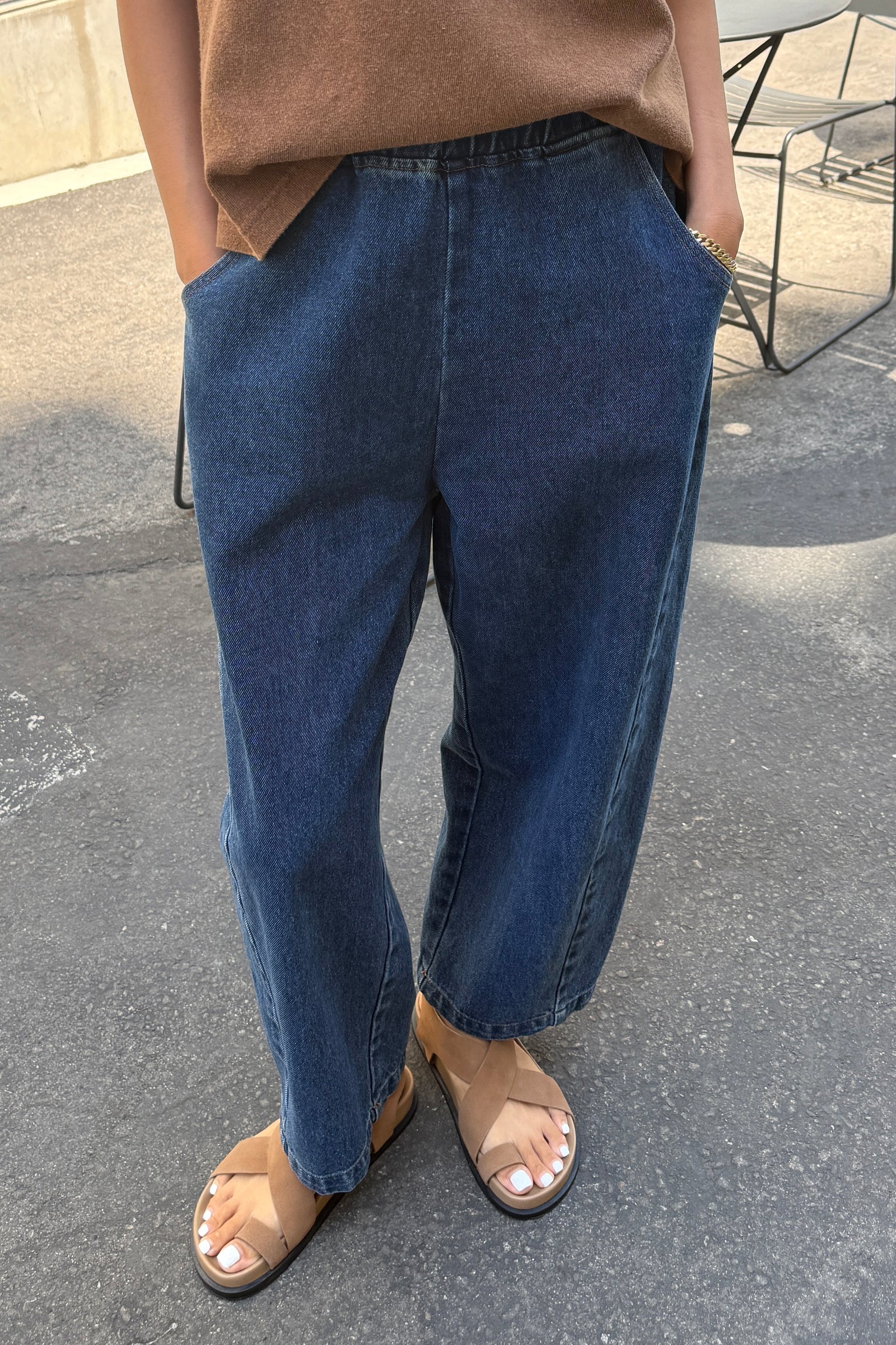Person wearing blue jeans and a brown top on a street.