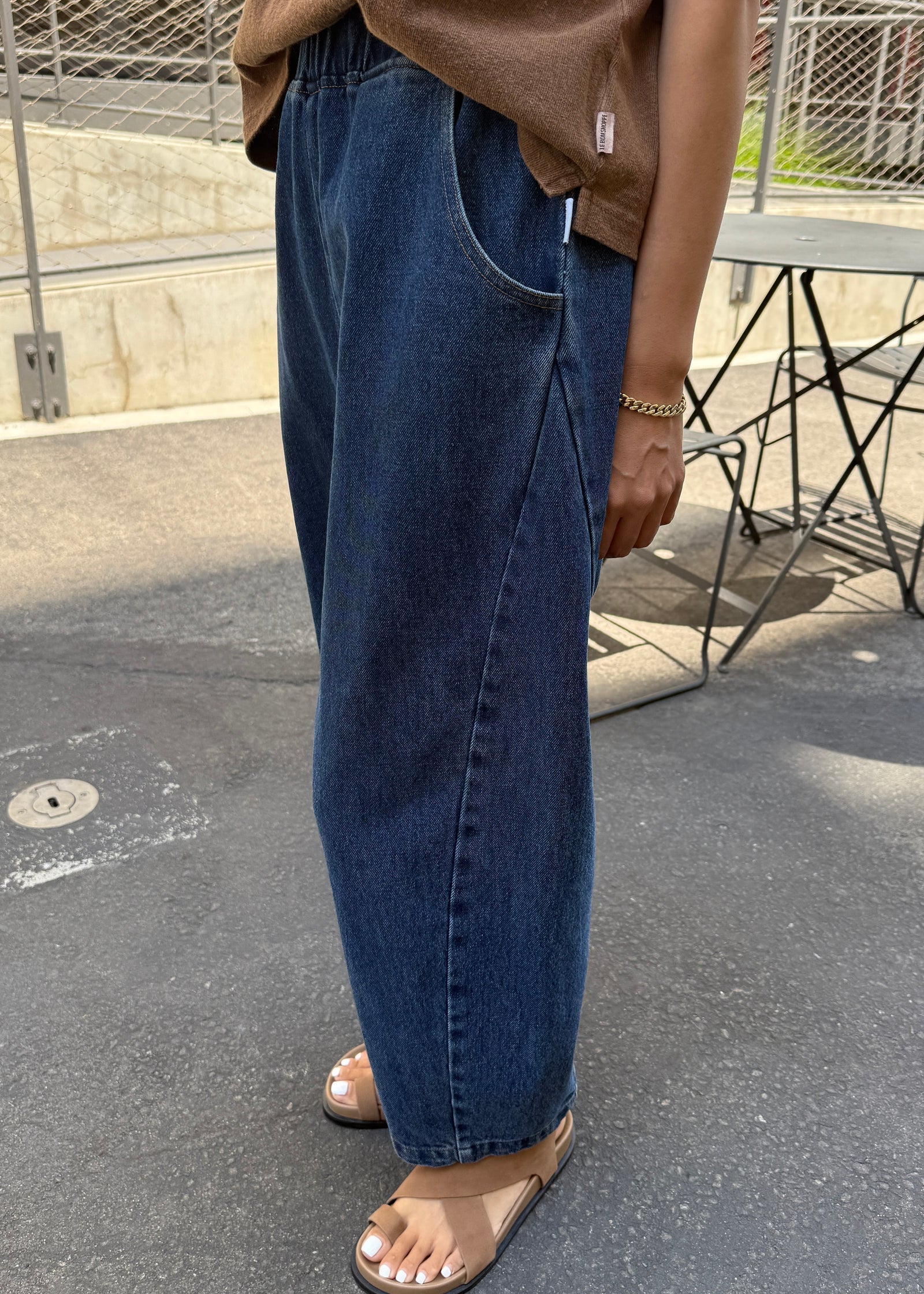 Person wearing blue jeans and a brown top on a street.