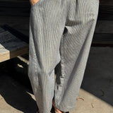 Person wearing white and blue striped wide-leg jeans and a yellow top on a concrete surface.