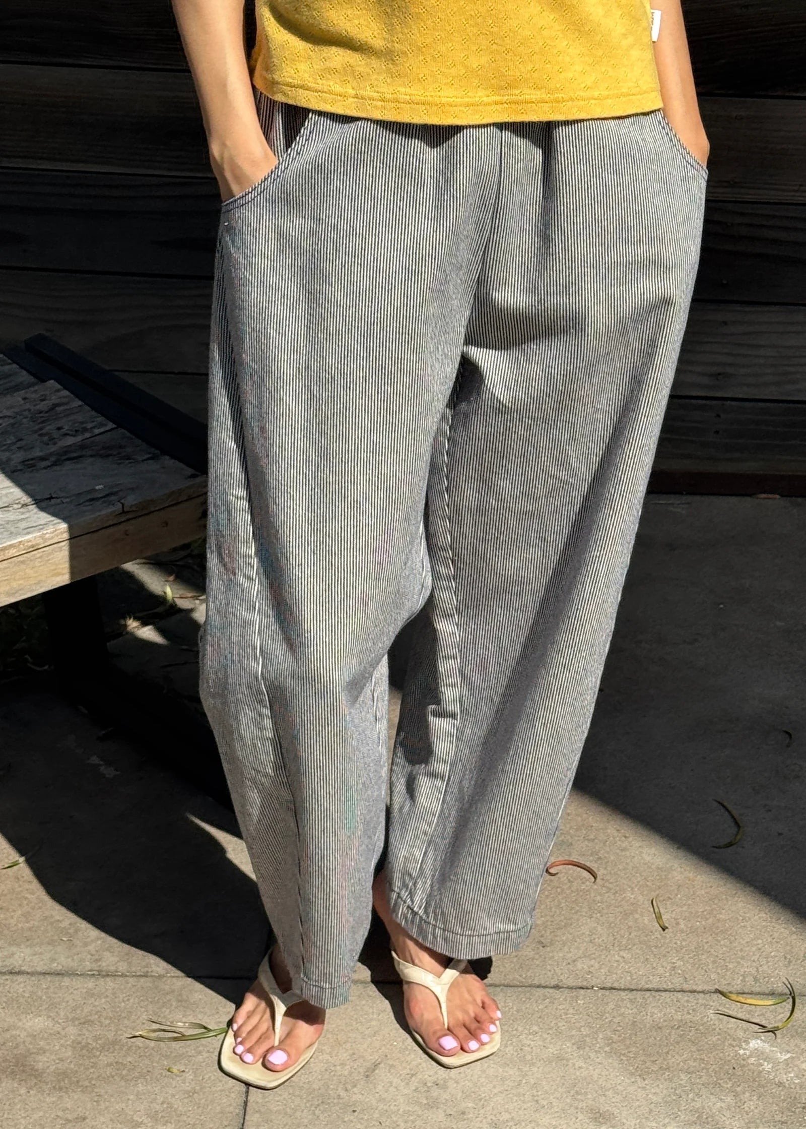 Person wearing white and blue striped wide-leg jeans and a yellow top on a concrete surface.