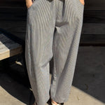 Person wearing a yellow top and white and blue striped wide-leg pants standing on a concrete surface.
