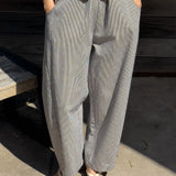 Person wearing a yellow top and white and blue striped wide-leg pants standing on a concrete surface.