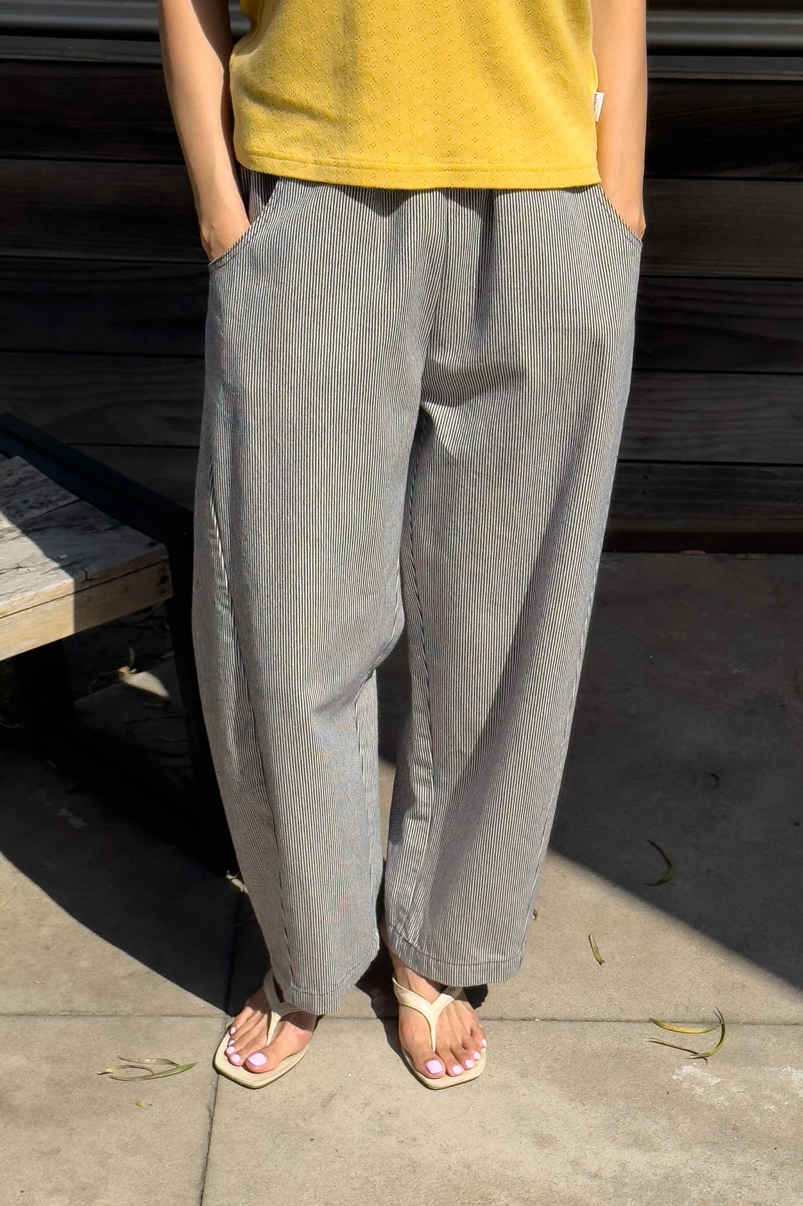 Person wearing a yellow top and white and blue striped wide-leg pants standing on a concrete surface.