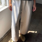 Person wearing a dark top and light-colored pants standing in a room with sunlight streaming in.