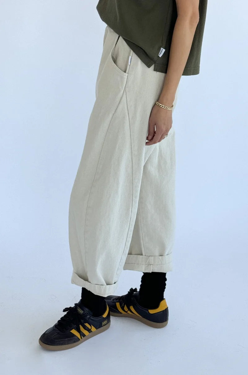 Person wearing beige wide-leg pants, black sneakers with yellow accents, and a grey top on a white background
