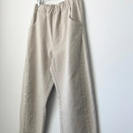 Beige pants hanging on a wooden hanger against a white wall
