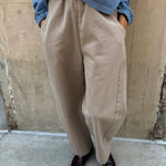 Person wearing beige pants and a blue shirt against a beige wall.