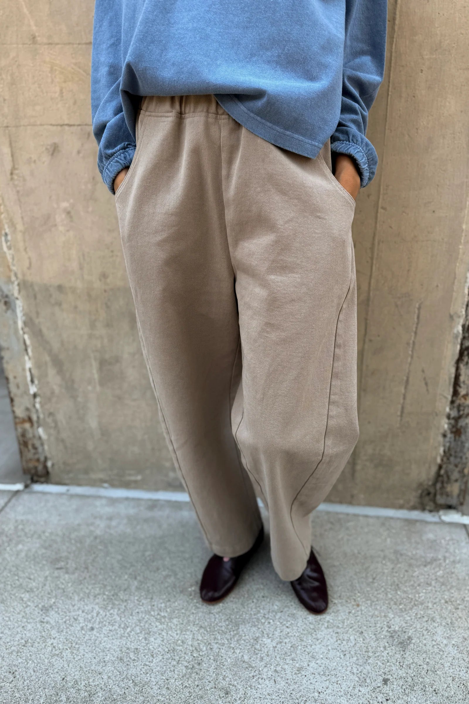 Person wearing beige pants and a blue shirt against a beige wall.