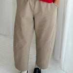 Person wearing a red top and beige pants with black shoes on a light background