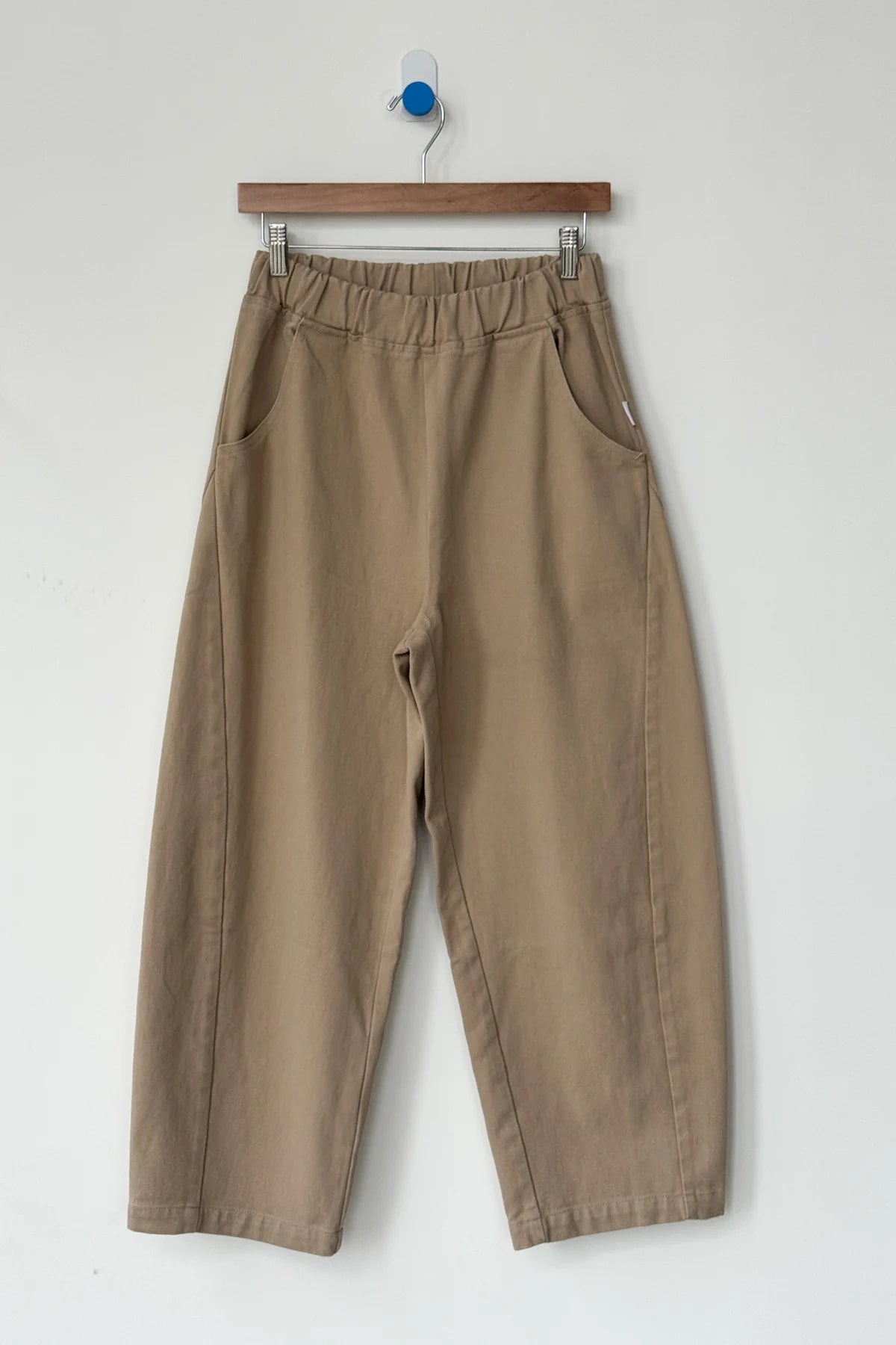 Brown pants hanging on a wooden hanger against a white background