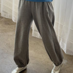 Person wearing gray sweatpants and a blue sweater with white shoes in front of a white curtain.