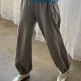 Person wearing gray sweatpants and a blue sweater with white shoes in front of a white curtain.