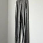 Gray sweatpants hanging on a wooden hanger against a white wall.