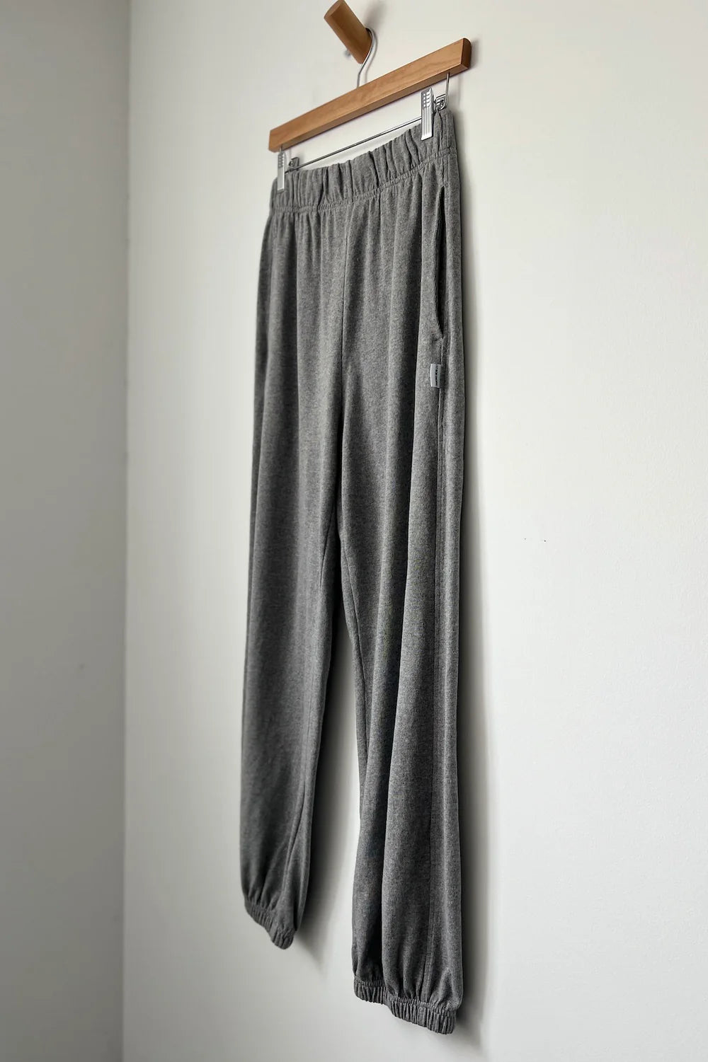 Gray sweatpants hanging on a wooden hanger against a white wall.
