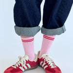 A pair of pink Boyfriend Socks with a double white stripe, worn with blue denim jeans and red sneakers.