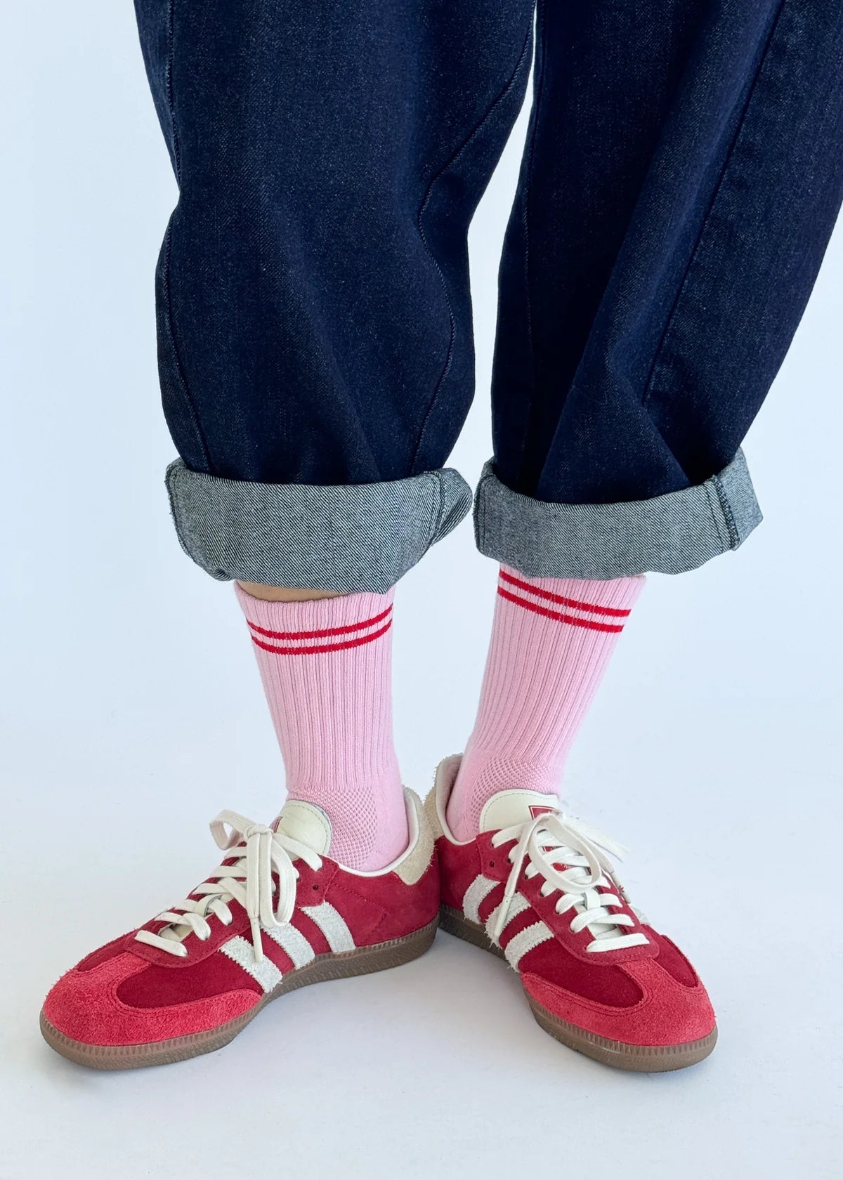A pair of pink Boyfriend Socks with a double white stripe, worn with blue denim jeans and red sneakers.