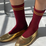 Red socks with gold stripes worn with gold shoes on a light background