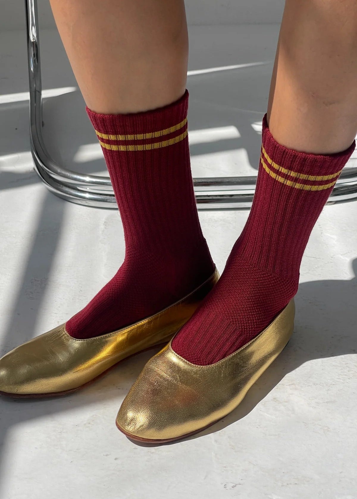 Red socks with gold stripes worn with gold shoes on a light background