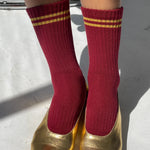 Red socks with gold stripes worn with gold shoes on a light background