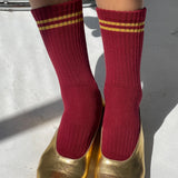 Red socks with gold stripes worn with gold shoes on a light background