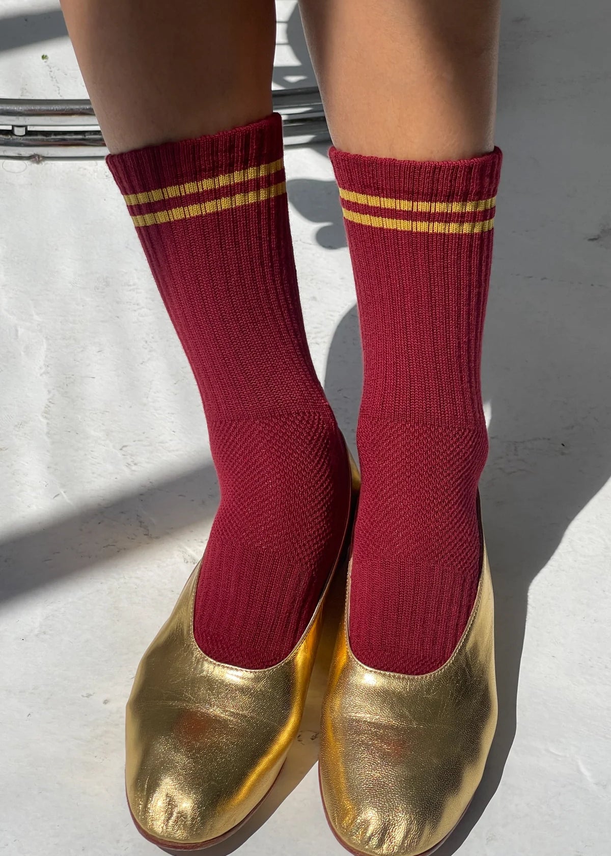 Red socks with gold stripes worn with gold shoes on a light background