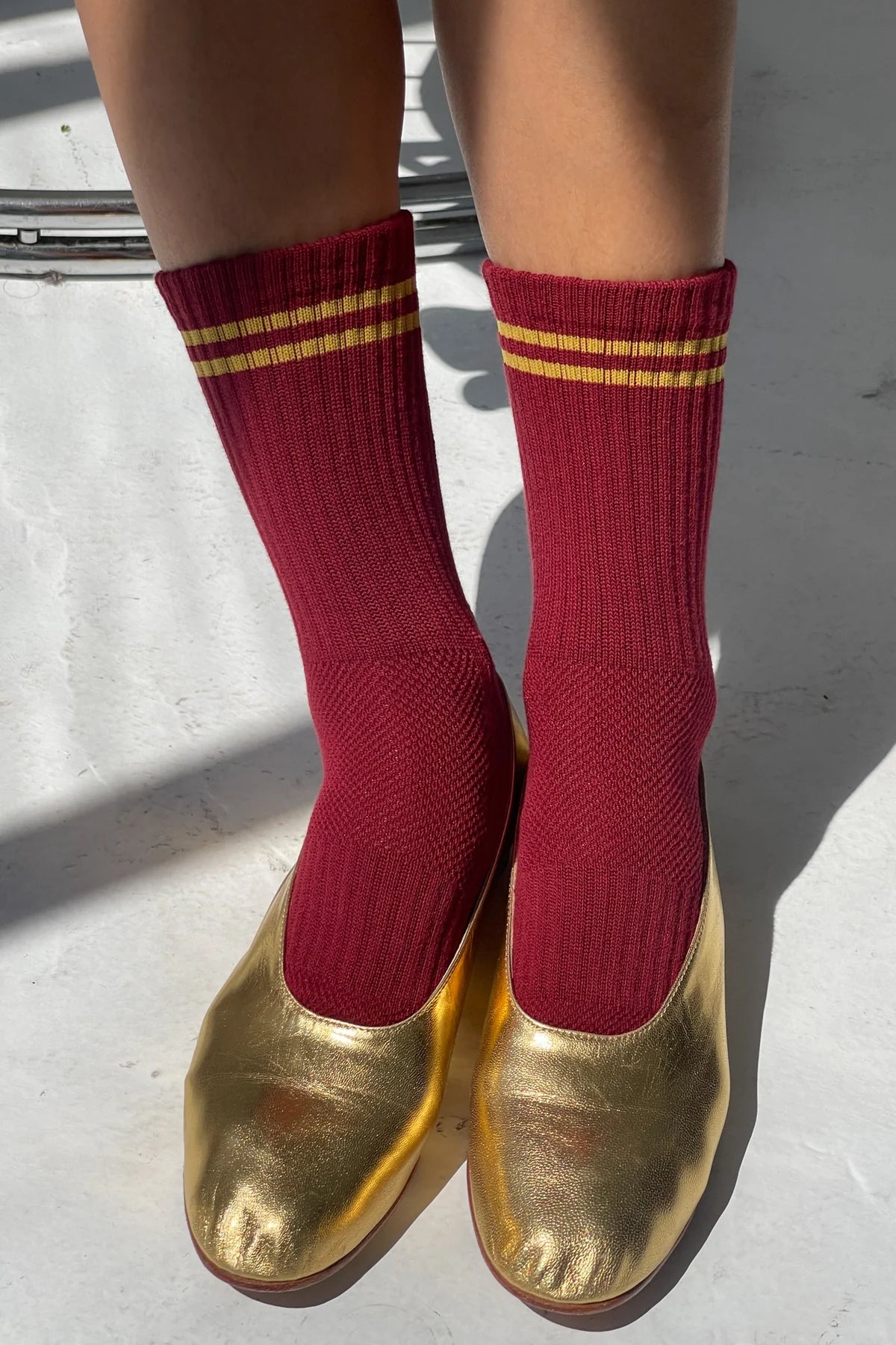 Red socks with gold stripes worn with gold shoes on a light background