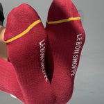 Red socks with yellow accents and 'Le Bon Shoppe' branding on a gray background