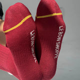 Red socks with yellow accents and 'Le Bon Shoppe' branding on a gray background