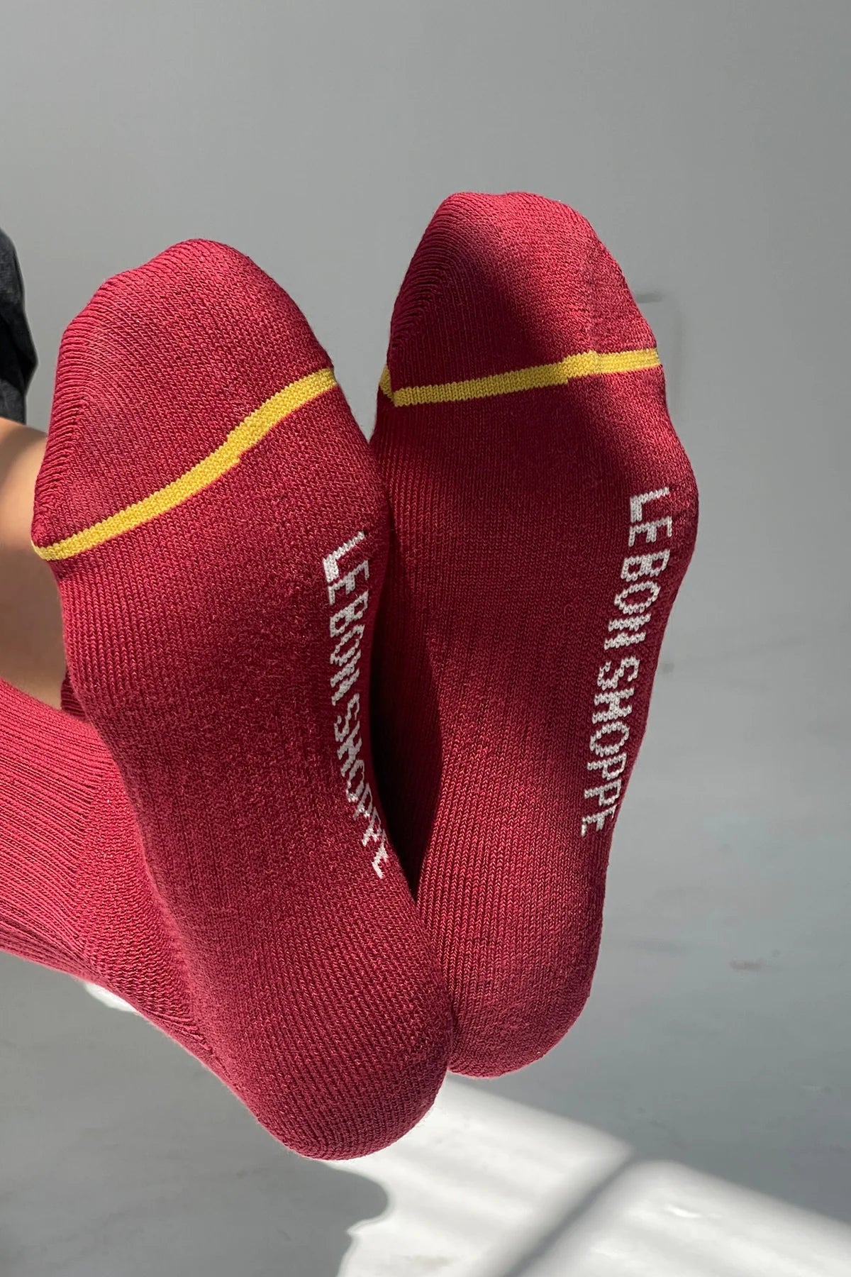 Red socks with yellow accents and 'Le Bon Shoppe' branding on a gray background