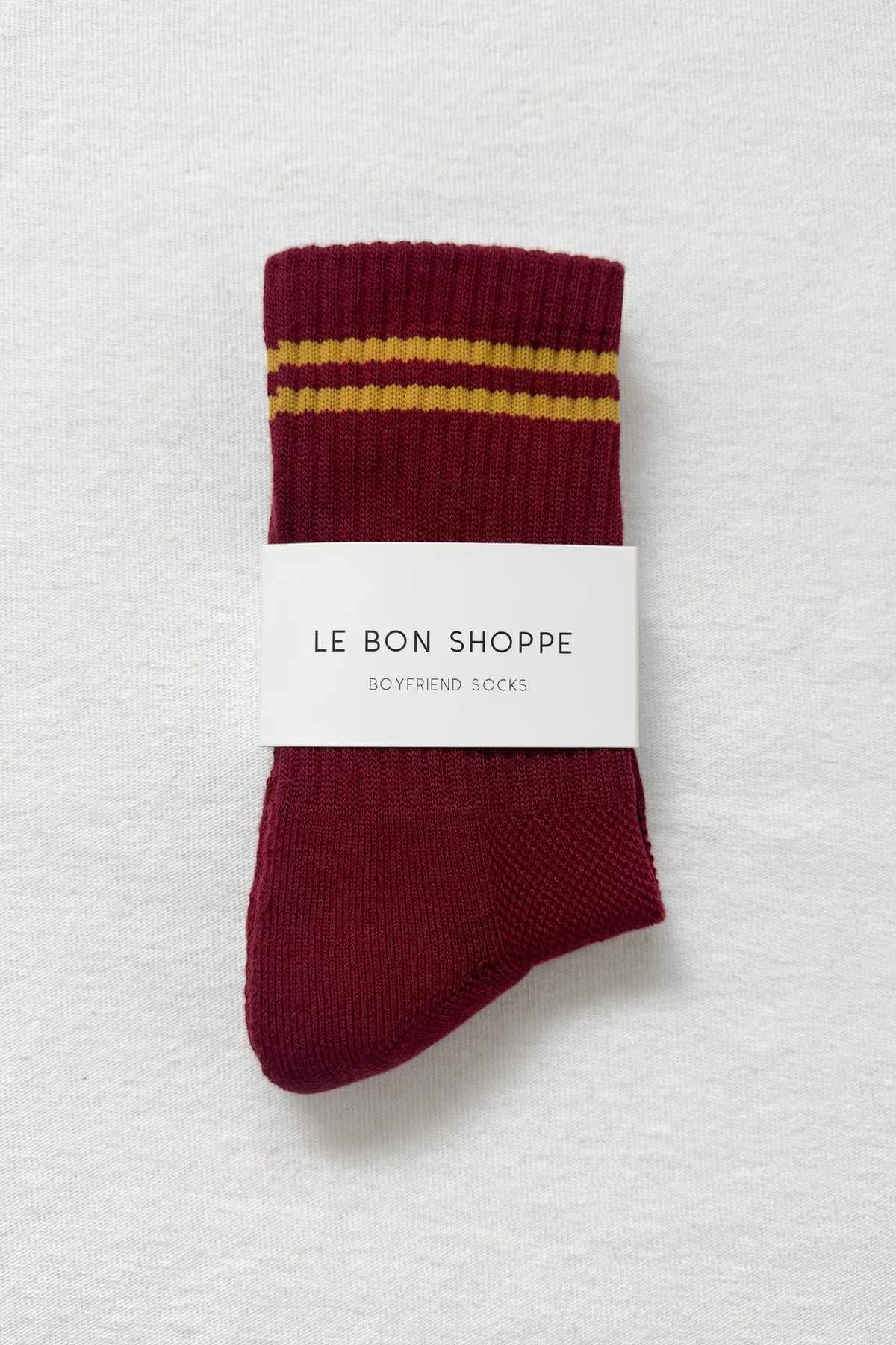 Maroon socks with yellow stripes on a white background, in Le Bon Shoppe packaging.