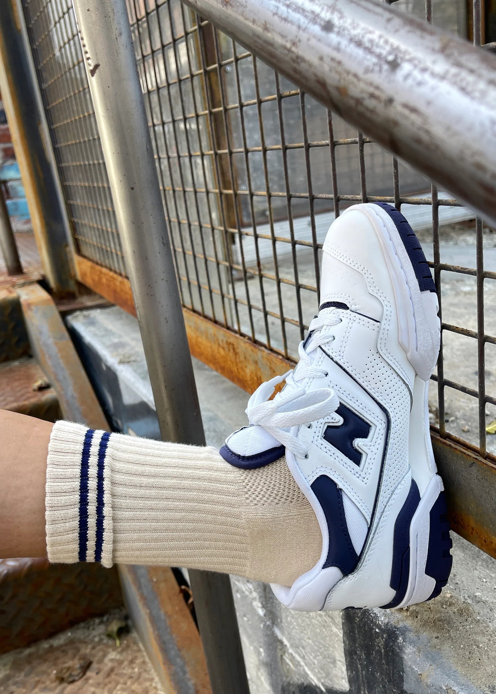 White and navy sneaker with a matching sock on a metal staircase.